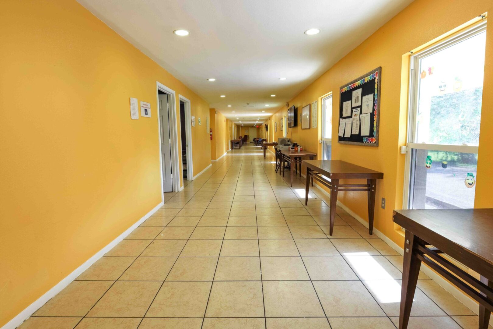 Bright hallway with yellow walls and tile flooring, featuring benches and bulletin boards.