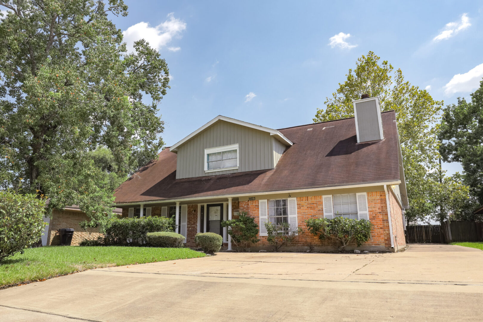 A brick house with a large porch and driveway under a clear blue sky.